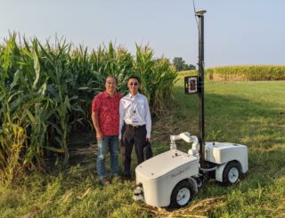 Dr. Lie Tang and Dr. Hongwei Zhang stand with PhenoBot in a corn field located within the ARA wireless testbed